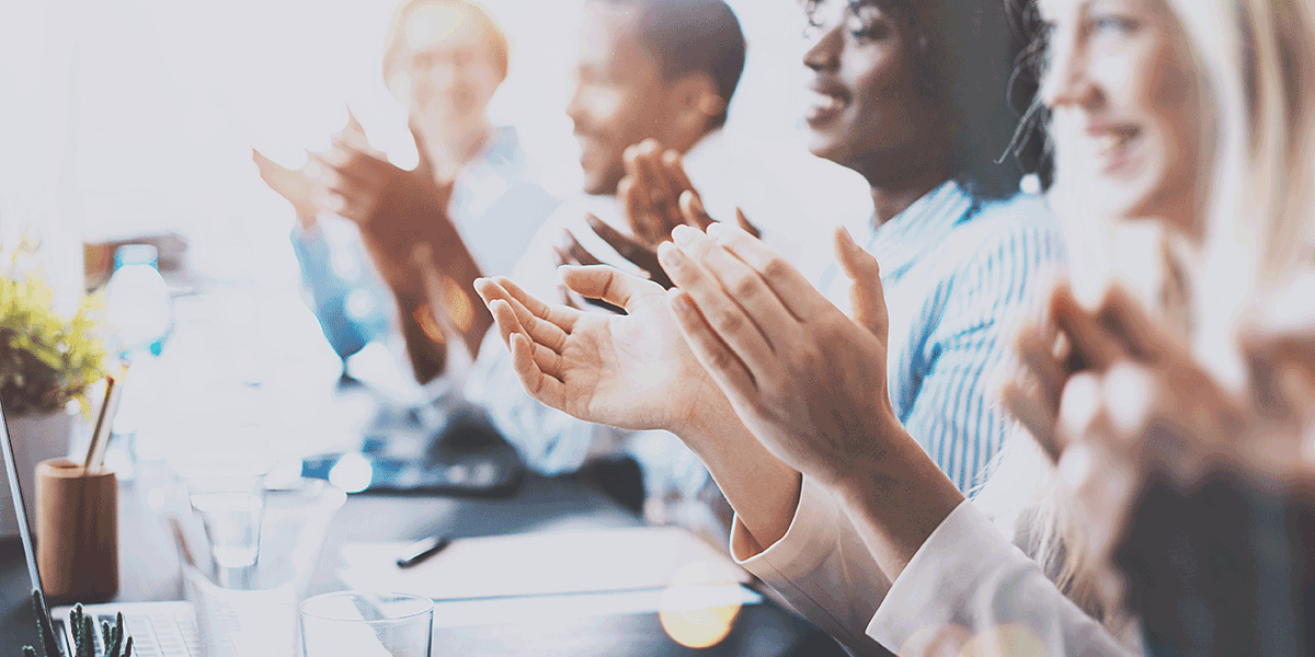 A group of businesspeople sitting at a table applaud.