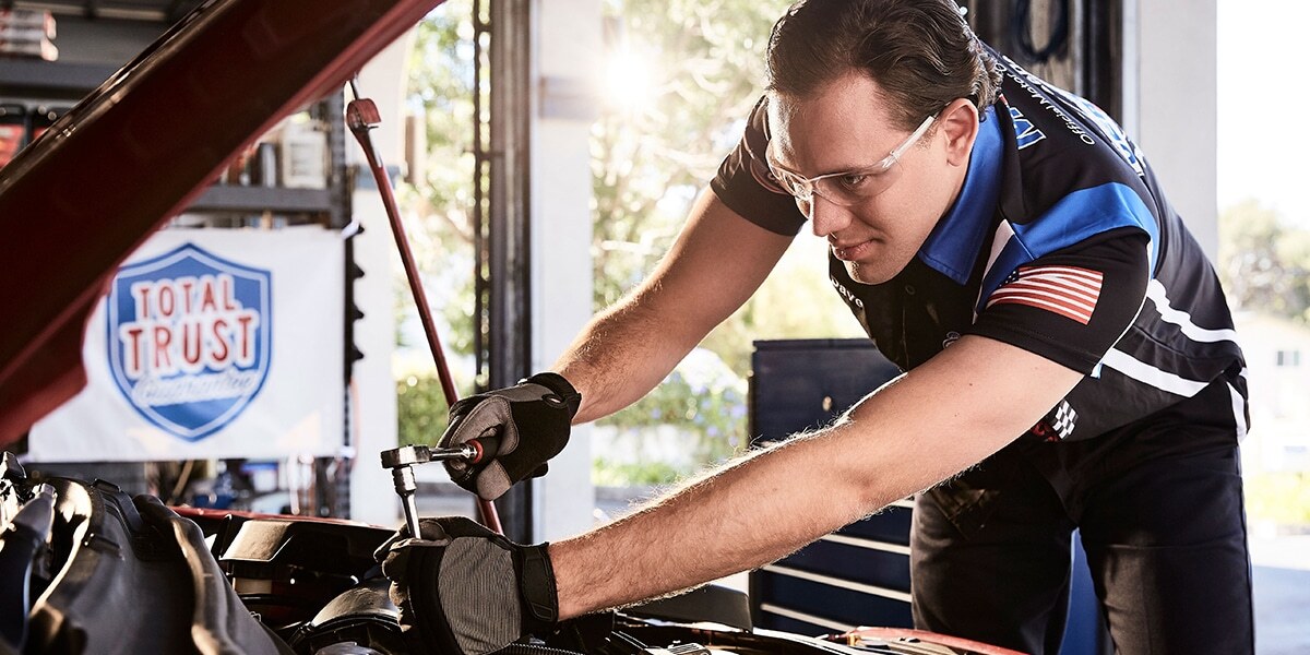 Technician works on car under its hood.