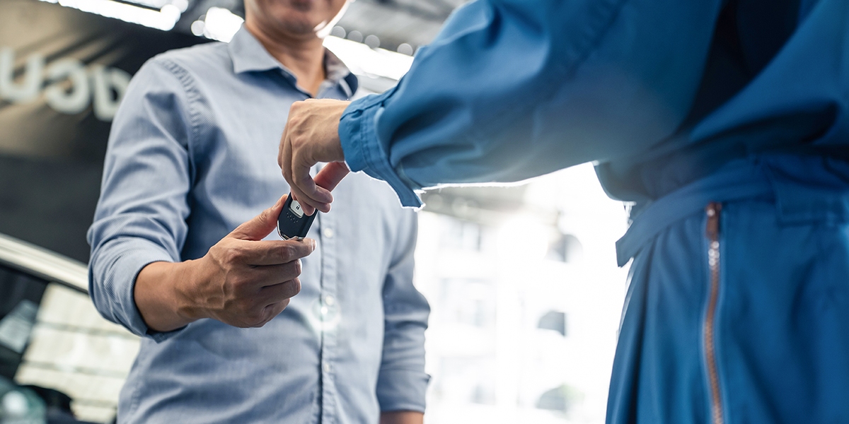 An auto franchise tech hands a car key to a customer.