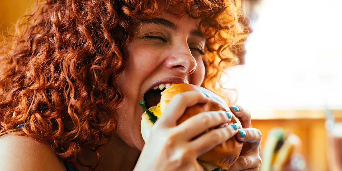 A girl with red hair is eating a cheeseburger.