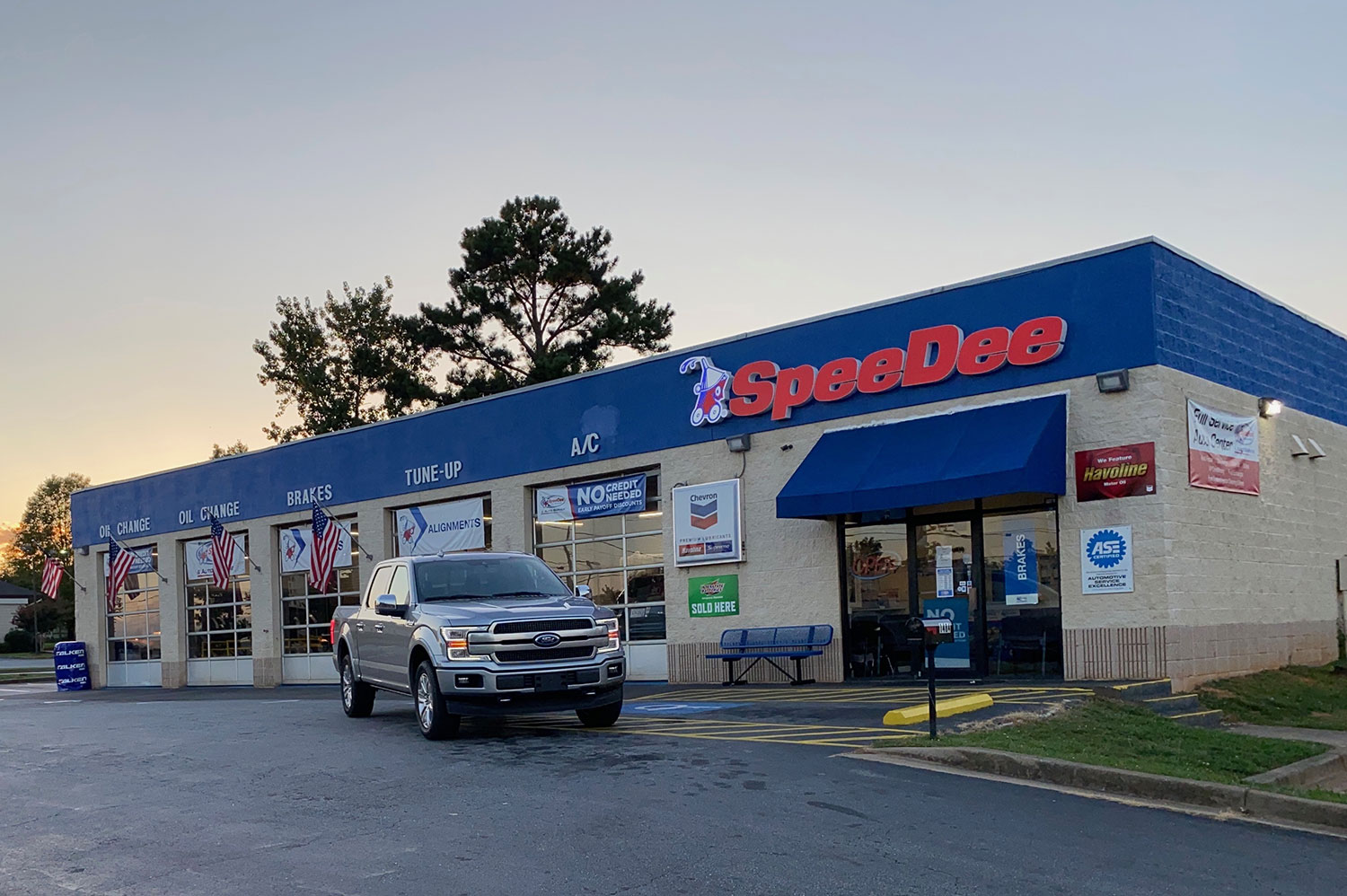 Exterior shot of a SpeeDee Oil Change & Auto Service center. A pickup truck is shown pulling away from one of the open service bays.