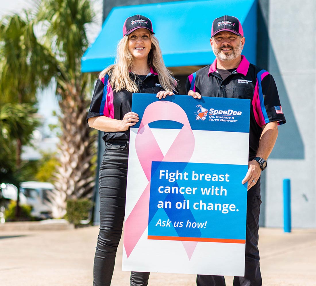 Two SpeeDee employees hold a sign about breast cancer awareness.