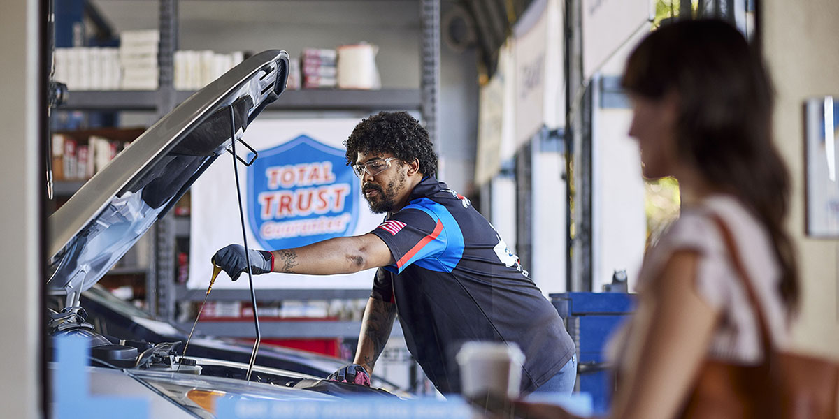 A SpeeDee technician does an oil change in the bay while a customer watches through a window in the lobby.